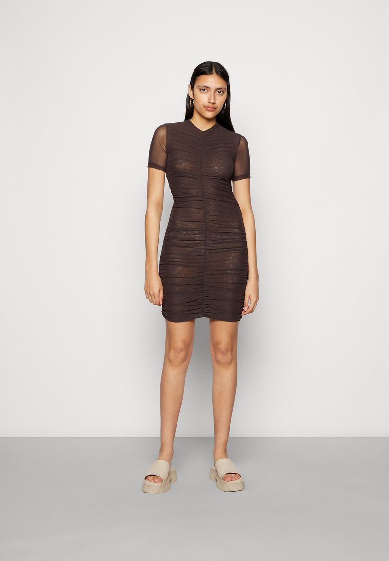 Vestido curto castanho com um design texturizado e franzido, e mangas curtas e transparentes. Modelo usa sandálias de plataforma bege, de pé contra um fundo neutro.