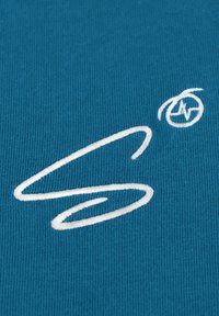 Teal stof met een wit geborduurd logo en ontwerp. Het materiaal heeft een textuur met een fijne ribbelpatroon over het geheel.