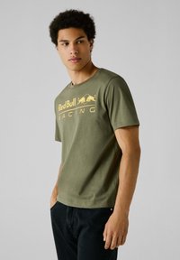 Olivno zeleni bombažni T-shirt s krožnim izrezom in kratkimi rokavi, ki na sprednji strani prikazuje rumen grafični tisk "Red Bull Racing".