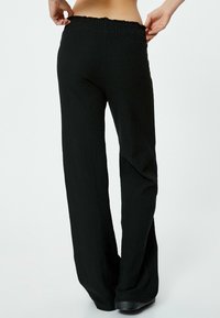 Pantaloni neri a gamba larga realizzati in un tessuto testurizzato, dotati di una vita elastica e una vestibilità morbida, con una superficie liscia e senza motivi visibili.