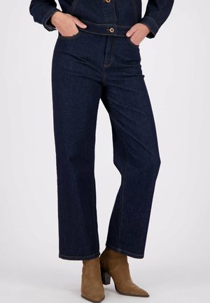 Donkerblauwe denim wijde broek met zichtbare stiksels en een hoge taille, gecombineerd met bruine enkellaarsjes. Voorzien van zijzakken en een ontspannen pasvorm.