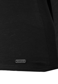 Schwarzes T-Shirt aus weichem Stoff mit einer subtilen Textur. Ein kleines, metallisches "Key Largo"-Etikett ist am unteren Saum angebracht.