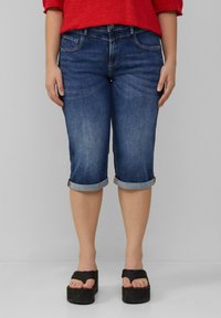 Donkerblauwe spijker capri broek met opgerolde manchetten, voorzien van voorzakken en subtiele vervaging. Gemaakt in combinatie met zwarte platform sandalen.