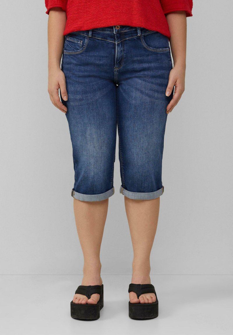 Donkerblauwe spijker capri broek met opgerolde manchetten, voorzien van voorzakken en subtiele vervaging. Gemaakt in combinatie met zwarte platform sandalen.