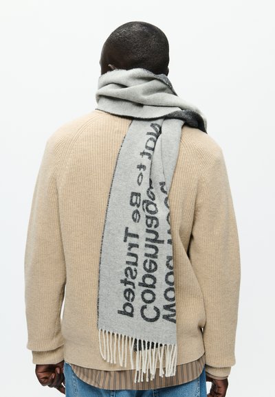 Hallide hallide kampsun, millel on must tekst, frantsiiside ääred, mis on mugavalt asetatud kaela ümber beežist tekstureeritud sviitri peale.