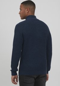 Jersey de punto de color navy con un cuello alto, tejido texturizado y puños acanalados. Presenta un ajuste ceñido y un diseño sin costuras en la parte posterior.