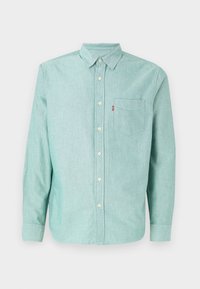 Camicia button-up in tessuto turchese chiaro, con colletto classico, maniche lunghe, taschino frontale e dettagli dei bottoni bianchi.