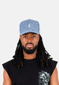 Denimkeps i ljusblå färg, broderad logotyp framtill, böjd skärm och strukturerat mönster. Svart ärmlös tröja under.