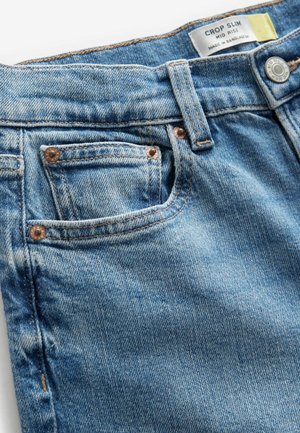 Jeans a sigaretta in denim blu chiaro, con rivetti in rame, vita media e una leggera sfumatura nella trama del tessuto.