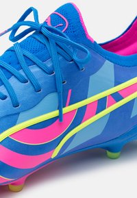 Scarpe da calcio sintetiche blu con accenti in rosa brillante e giallo. Presentano un materiale testurizzato, motivi curvi e un sistema di allacciatura audace.