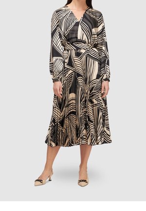 Femme portant une robe midi beige et noire à motifs géométriques, manches longues, et des escarpins beiges à bout pointu avec détail chaîne.