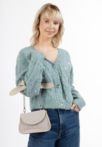 Grøn strikket cardigan med store knapper, parret med en kviltet beige håndtaske med kædestrop og læderdetaljer.
