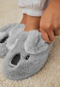 Grå koala-tema hjemmesko lavet af blød kunstpels, med sorte detaljer til øjne og næse samt hvide øredetaljer.