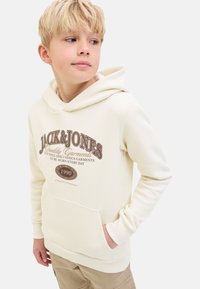 Hoodie crème en tissu doux avec une poche avant. Dispose d'un imprimé graphique marron avec du texte et d'une capuche à cordon.