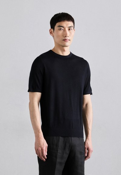 Pull noir à manches courtes en maille douce, avec un col rond et une silhouette ajustée, associé à un pantalon foncé.