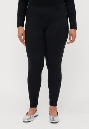 Sorte leggings med en glat tekstur, med en række nitter langs de ydre sømme. Bæres med sølvfarvede flade sko.