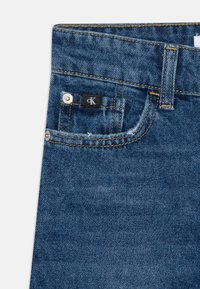 Mörkblå denimjeans med kontrasterande gul sömnad, med en liten svart etikett och en metallknapp på framfickan.