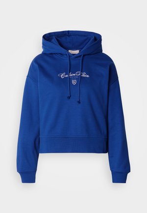 Sinine lühendatud pusa pehme kangaga, millel on nööriga kapuuts ja valge tikandiga logo keskel. Soonilised varrukaserval ja äärel.