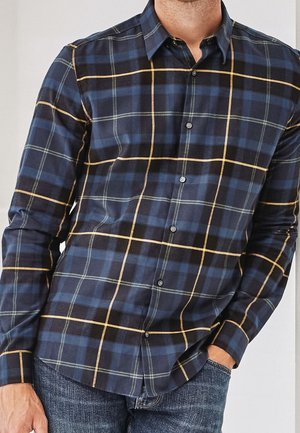 Chemise à carreaux bleu marine avec des lignes vertes et jaunes, à manches longues, devant boutonné et col étalé. Fabriquée en tissu doux.