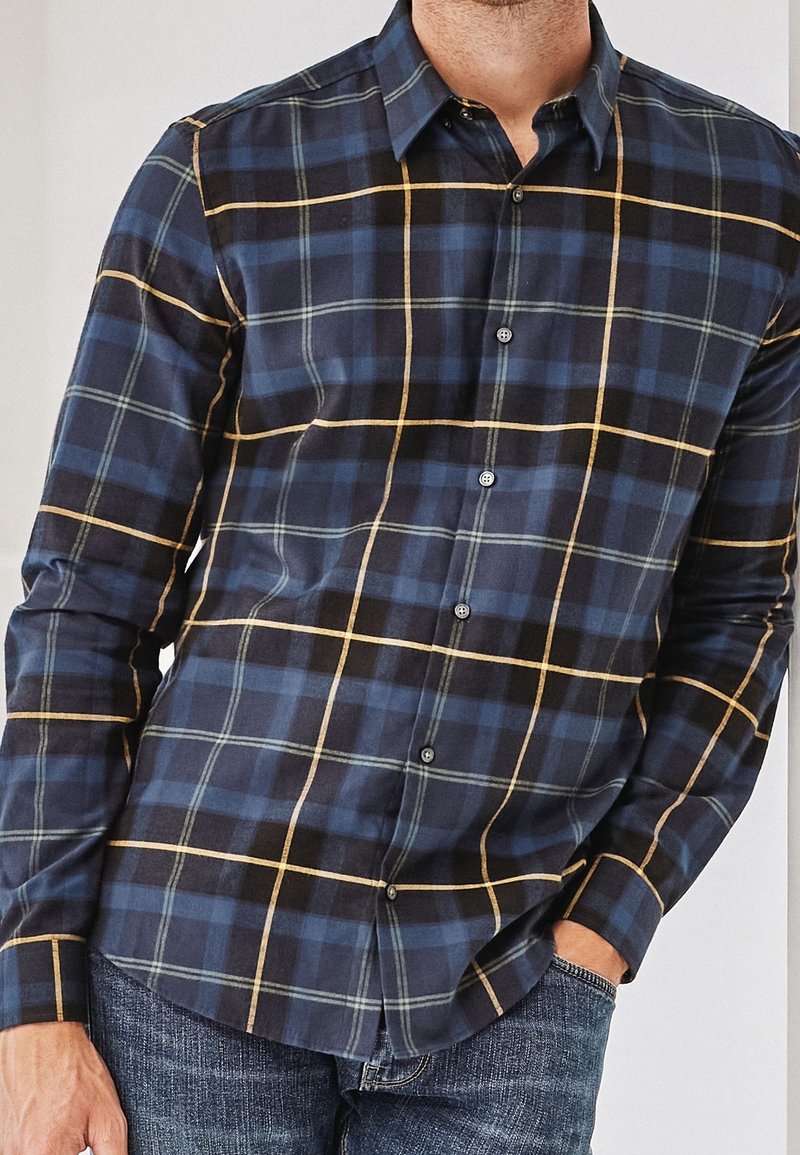 Chemise à carreaux bleu marine avec des lignes vertes et jaunes, à manches longues, devant boutonné et col étalé. Fabriquée en tissu doux.