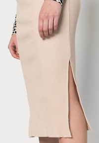 Beige, knielanger Ripprock mit seitlichen Schlitzen, der eine weiche Textur und diskrete Saumdetails aufweist.