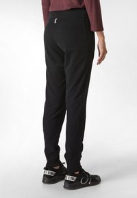 Zwarte joggingbroek met een aansluitend ontwerp, elastische tailleband en geribbelde boorden. Glad textuur en zichtbare zijna seams; gedragen met zwarte sportschoenen.