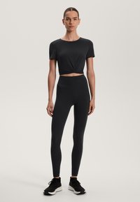 Fekete, rövid ujjú, cropped póló, elől csomózva. Fekete leggings derékvonalban magas szabású. Fekete sportcipők fehér talppal.