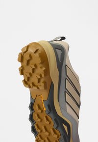 Sporta apavi ar beigu augšdaļu, pelēkiem akcentiem un strukturētu gumijas zoli ar izteiktu protektoru rakstu. Iekļauts vilkšanas cilpa.