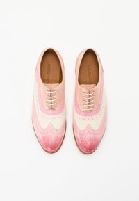 Scarpe in pelle rosa e crema con perforazioni decorative, design wingtip e finitura liscia, dotate di sei occhielli e lacci piatti.