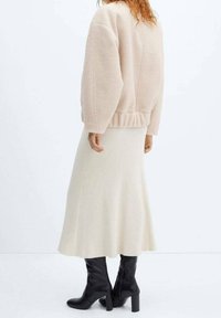Oversized beige fleece jacket with gathered waist, paired with a cream ribbed skirt and knee-high black heeled boots.