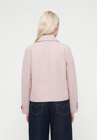 Ροζ σακάκι από μείγμα μαλλιού με φαρδιά γιακά, εφαρμοστή σιλουέτα και μανσέτες με κουμπιά. Το πίσω μέρος διαθέτει καθαρό, μινιμαλιστικό σχέδιο.