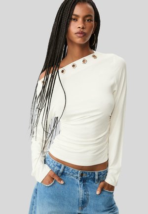 Weißes Langarmshirt mit einem freigelegten Schulter, ausgestattet mit Metallösen-Details entlang des Halsausschnitts. Glatte Textur, taillierte Passform.