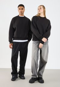 Sorte bomullsgenser med ribbede mansjetter, kombinert med sorte joggebukser og grå vide jeans. Klumpete svarte sko med teksturerte såler.