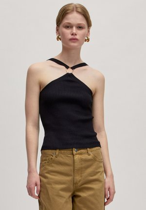 Zwarte geribbelde haltertop met een driehoekige vorm, voorzien van een gouden ringdetail bij de halslijn en dunne bandjes. Draagt met beige broeken.