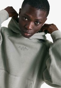 Világoszöld kapucnis pulóver elülső zsebbel és hímzett logóval. Puha tapintású, kényelmes szabású, húzózsinóros kapucnival.