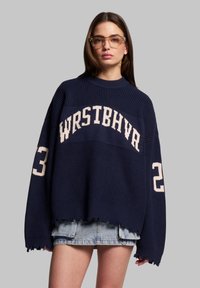Maglione navy oversize con texture a coste, con scritta in maglia bianca "WRSTBHVA" e numero "23" sulle maniche. Dettaglio orlo sfrangiato.