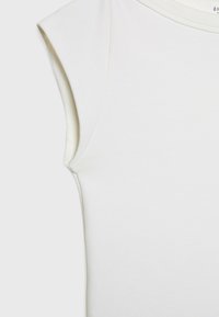 Krupni plan bijelog topa bez rukava koji prikazuje lijevo rame s okruglim izrezom i glatkom teksturom tkanine.