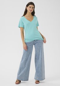 Světle modré tričko s krátkým rukávem a výstřihem do V vyrobené z měkké látky v kombinaci s širokými džíny v světle modré. Celkový vzhled doplňují ploché hnědé sandály.