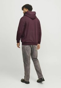 Bordeaurotter Hoodie mit großer Kapuze, gerippten Bündchen und Saum, kombiniert mit verwaschenen grauen Jeans und schwarzen Schuhen. Das Design ist lässig und entspannt.