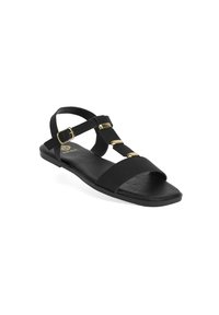 Black sandal featuring textured fabric straps, gold accent details, open toe design, and a flat sole. Minimalist style with adjustable ankle strap.