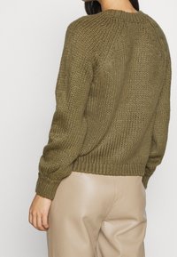 Sweter z dzianiny w kolorze oliwkowej zieleni o prążkowanej fakturze, z okrągłym dekoltem i lekko luźnym krojem. Długie rękawy i dopasowane prążkowane wykończenie u dołu.