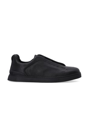 Black leather slip-on shoes with a textured finish, rounded toe, and a thick black rubber sole. Minimalist design with no laces.
