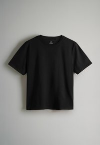 T-shirt noir à manches courtes et col rond suspendu contre un mur gris clair, vue de face avec une texture de tissu lisse et unie.