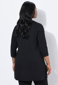 Schwarze Tunika mit dreiviertel Ärmeln, seitlichen Schlitzen und lockerer Passform. Glattes, weiches Material mit klassischem Design, das sich gut zum Übereinandertragen eignet.