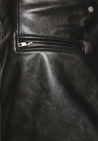 Vêtement en cuir noir avec une poche zippée dotée de quincaillerie en argent, texture lisse et vue en gros plan mettant en avant les détails et le brillant.