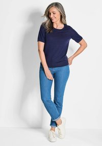 Marineblaues T-Shirt mit kurzen Ärmeln und Rundhalsausschnitt, kombiniert mit engen blauen Jeans und weißen Sneakers, mit einem lockeren Schnitt und weichem Material.