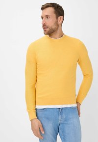 Gelber, gestrickter Pullover mit Rundhalsausschnitt, aus einem weichen Material gefertigt. Verfügt über lange Ärmel und einen figurbetonten Saum, kombiniert mit hellblauen Jeans.
