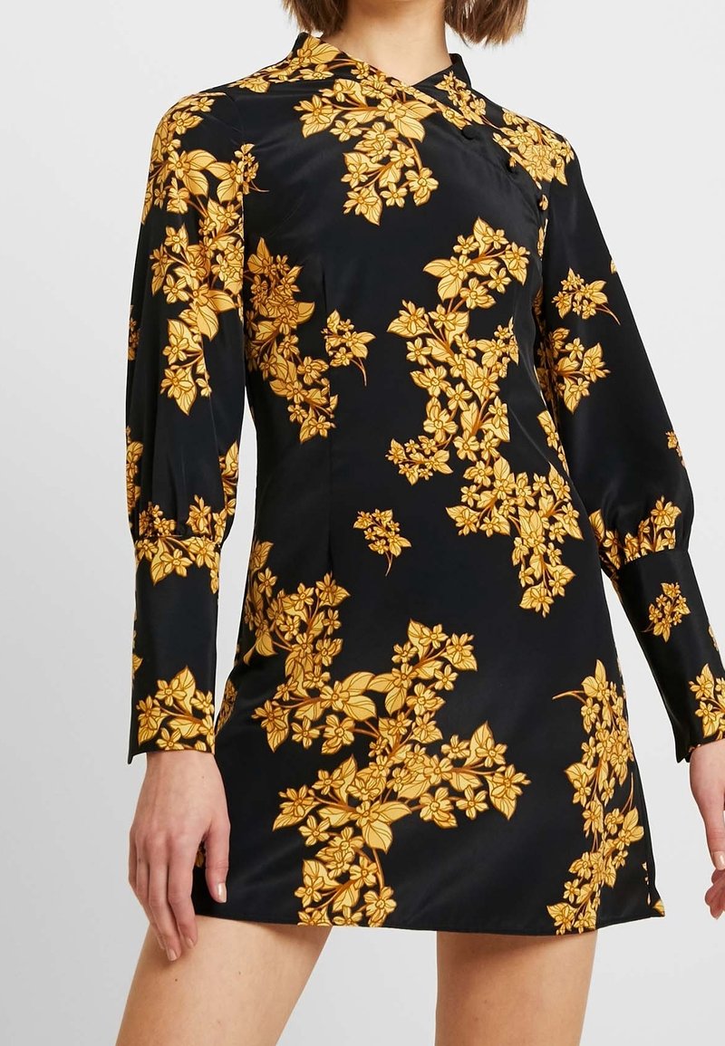 Robe noire à manches longues, arborant un motif floral jaune, une texture lisse et une silhouette ajustée, mettant en valeur un design moderne.