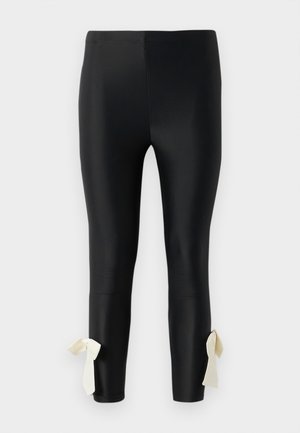 Leggings pretas feitos de material liso, com uma textura suave e laços em tom creme no tornozelo para um detalhe adicional.