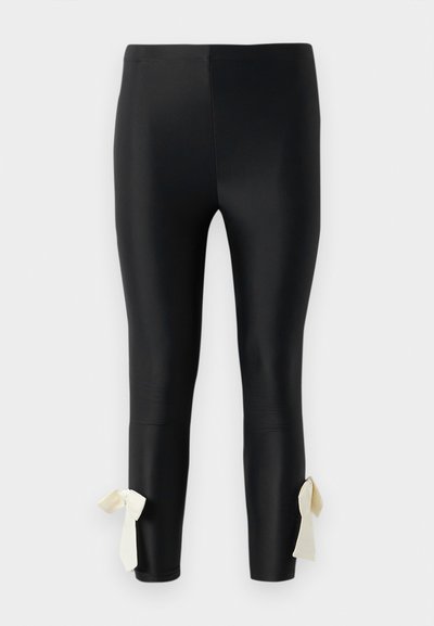 Črne legice iz gladkega materiala, z gladko teksturo in kremnimi trakovi za zavezovanje okoli gležnjev za dodatno podrobnost.